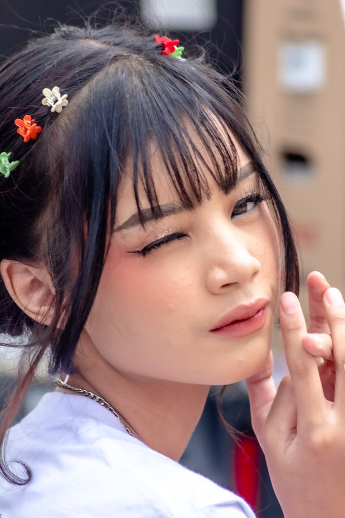 Close-up portrait of a young woman with floral hair clips winking playfully. Ideal for lifestyle and fashion themes.
