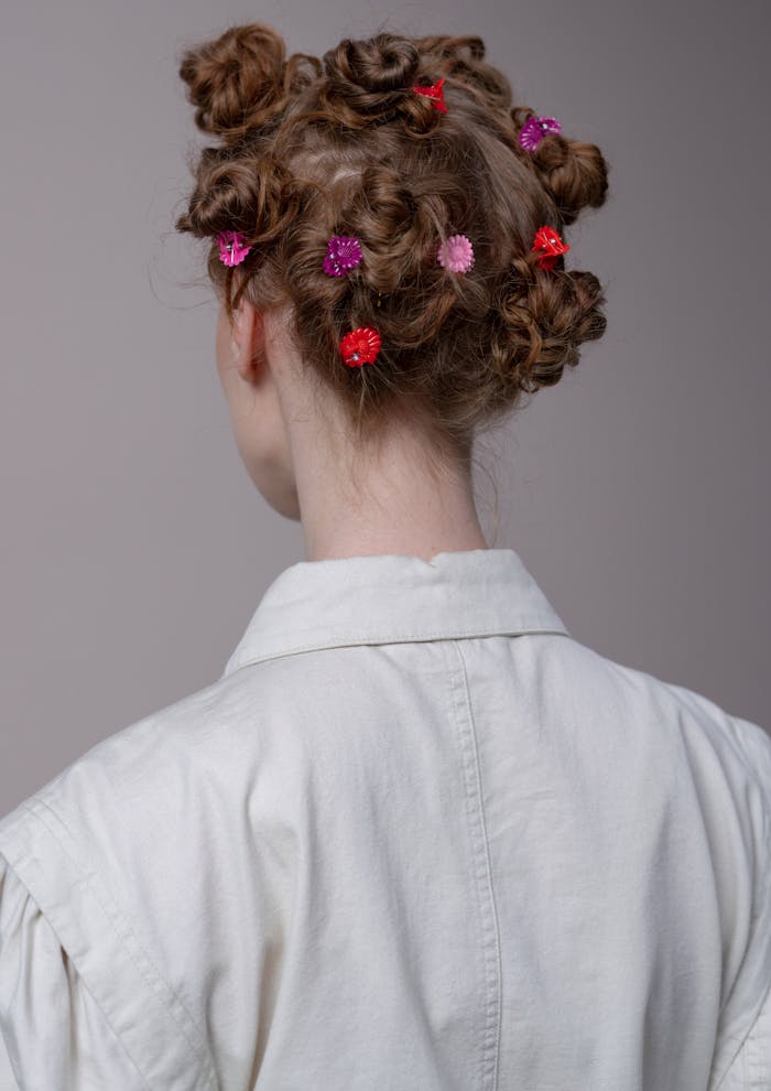 Close-up of a woman with creative hairstyle adorned with colorful hair clips against a gray background.